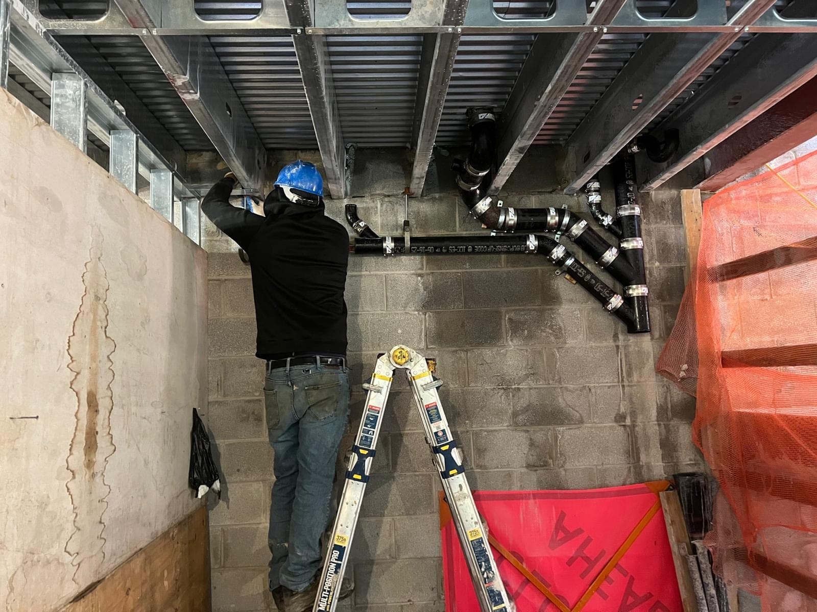 PLUMBON24 plumber installing drain and vent piping overhead during a commercial build-out